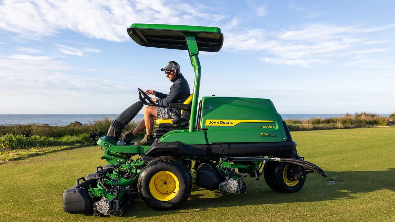 A man driving a green professional fairway mower on a golf course.