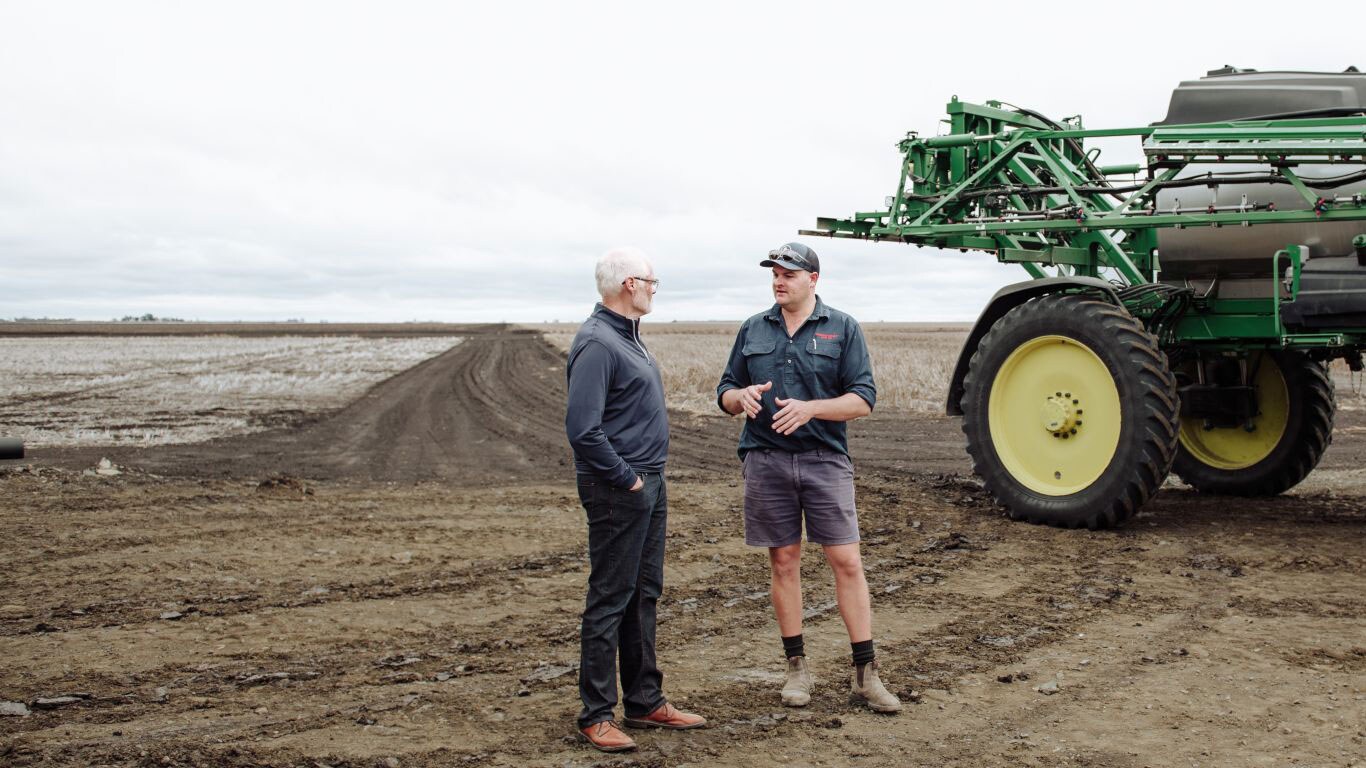 Two men talking in a ploughed paddock.