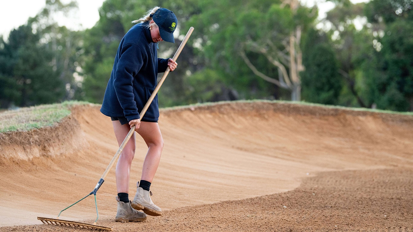 Women in Turf volunteer, Emma Lewis rakes bunker.