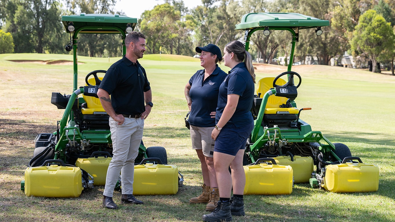 Corey Clark, standing with Chrissy Wilson and Olivia Cowan with John Deere mowers in background.