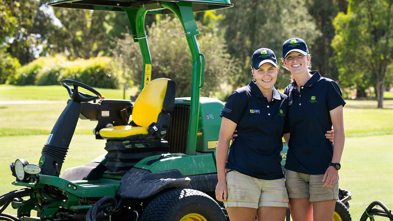 Two female volunteers from 2024 program standing in front of stationary fairway mower.