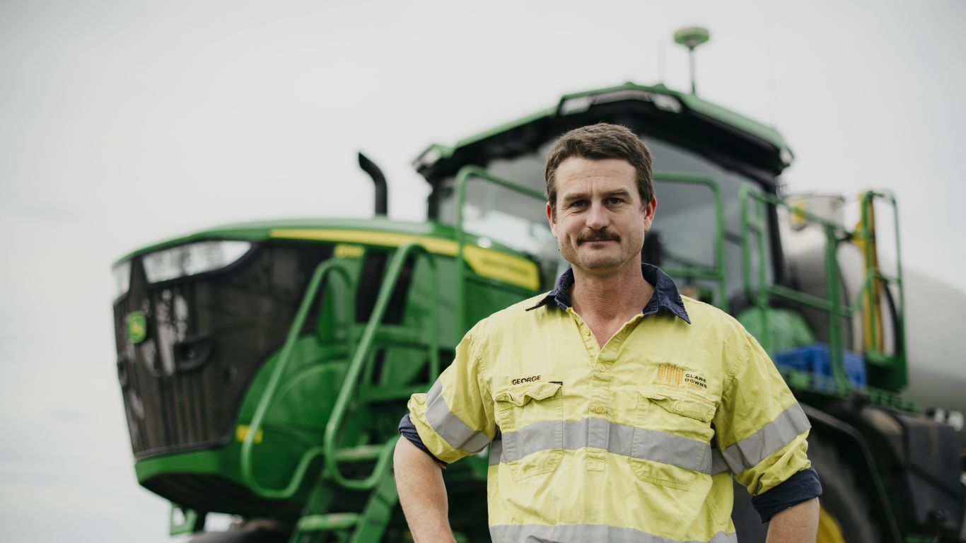 Person wearing a high‑visibility shirt standing in front of a large green tractor.