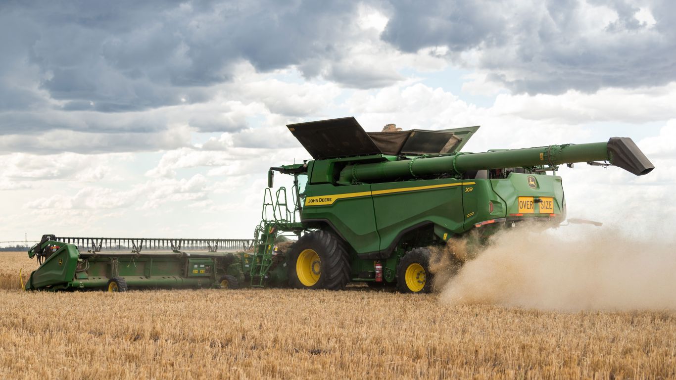 Large green machine with yellow wheels harvesting crop with dust and moody cloud