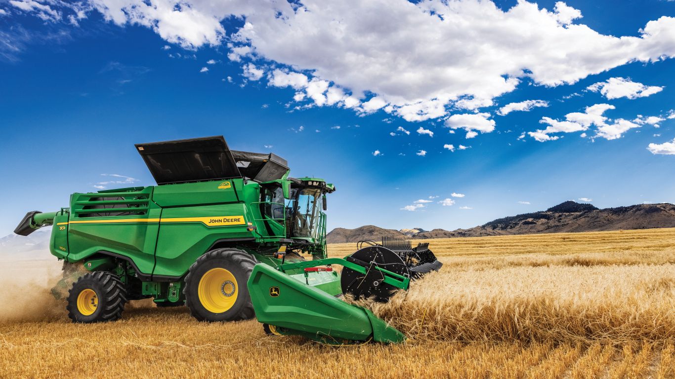 Large green combine in crop with blue sky
