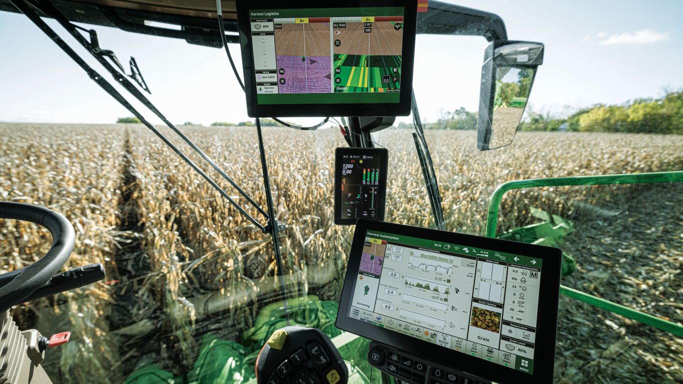 Inside the cab of combine looking out at crop with two screens