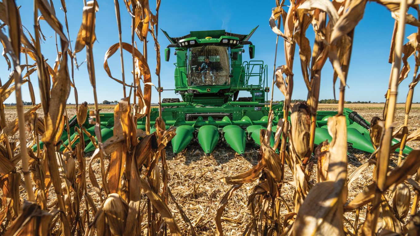 Front end of large green combine through crop with blue sky