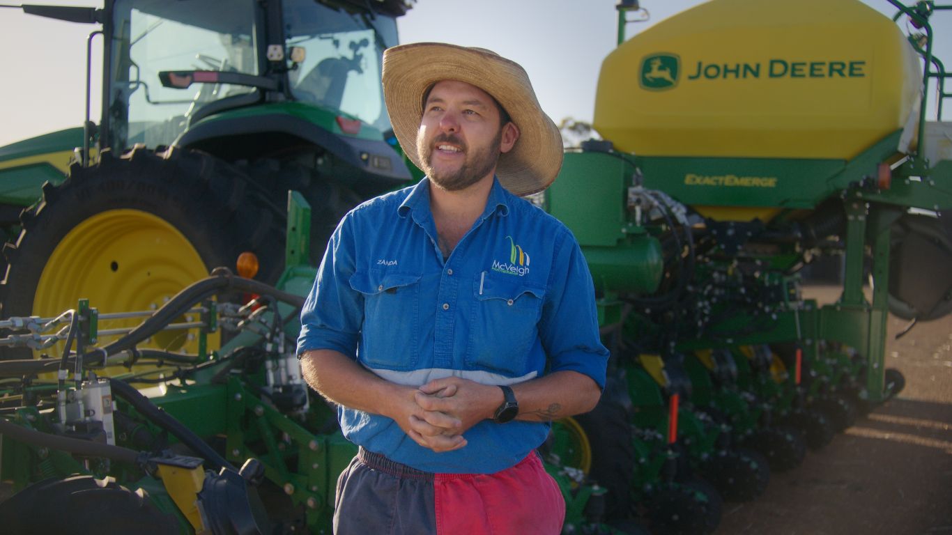 Man in blue shirt and hat in front of green and yellow machine.
