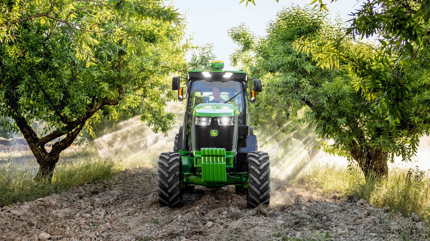 Green John Deere tractor in the middle of two green trees and rocky ground