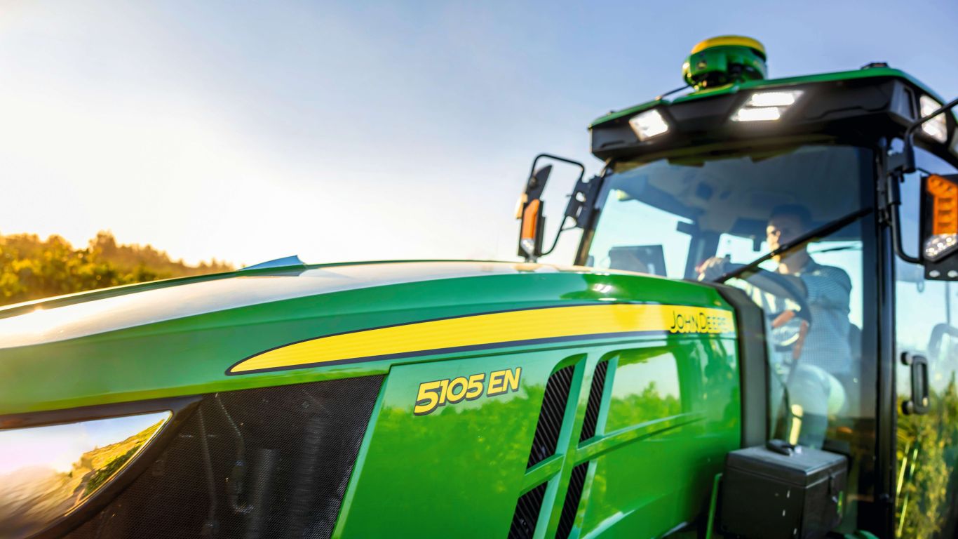 Front of green and yellow 5105 EN John Deere Tractor with male driver in the cab