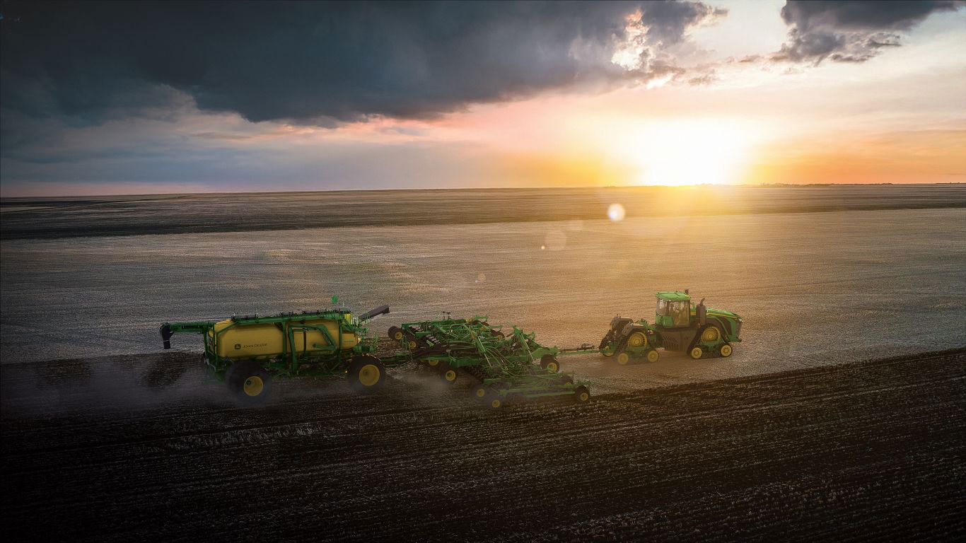 Birdseye view of large three piece green and yellow machine with black and yellow wheels in paddock with stormy sky.