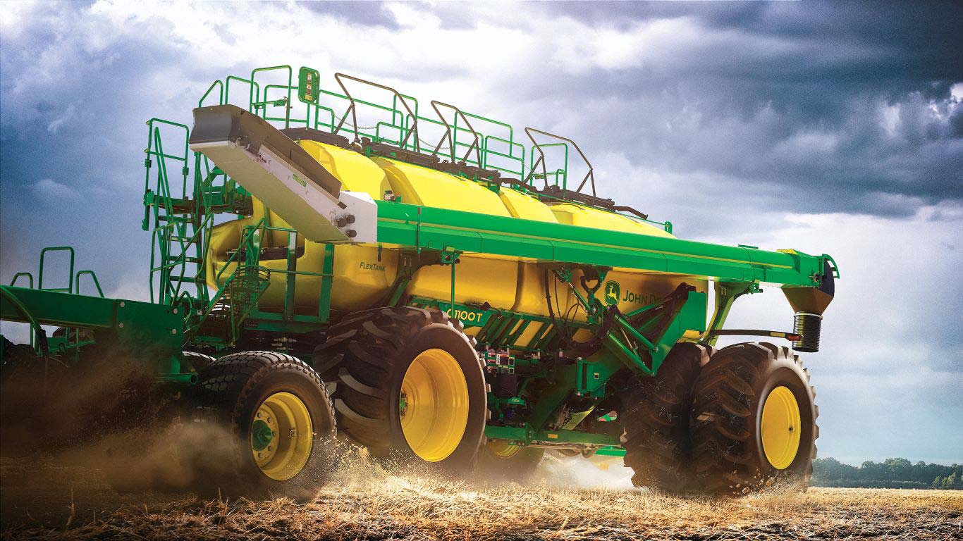 Side of large green and yellow machine with black and yellow wheels in paddock with stormy sky