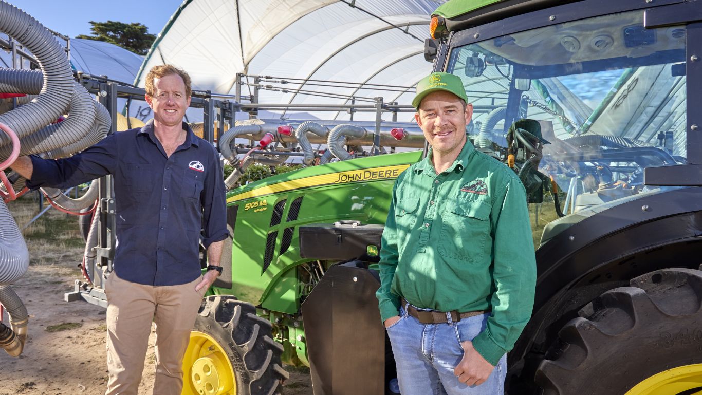 Two men beside a green John&nbsp;Deere tractor near tunnels