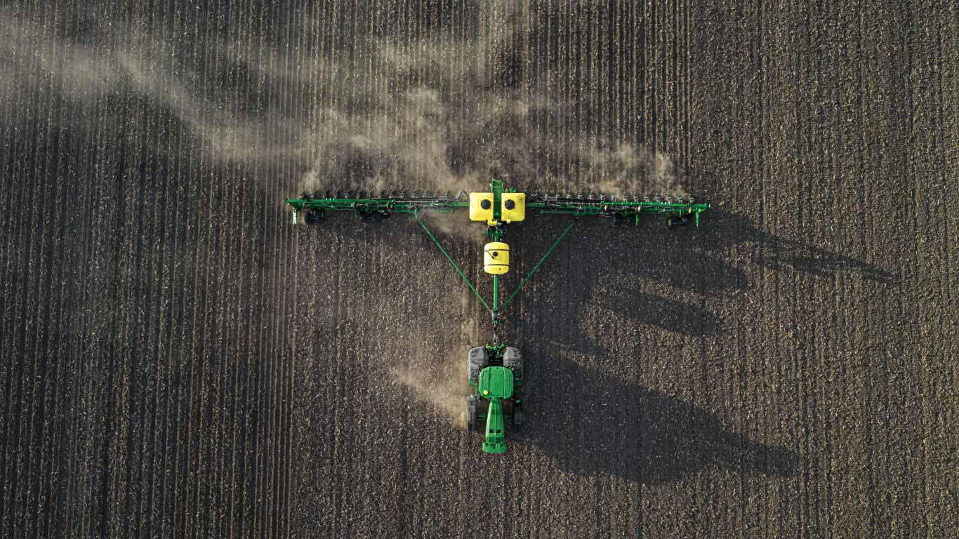 Birds eye view of a green tractor pulling a planting machine in soil