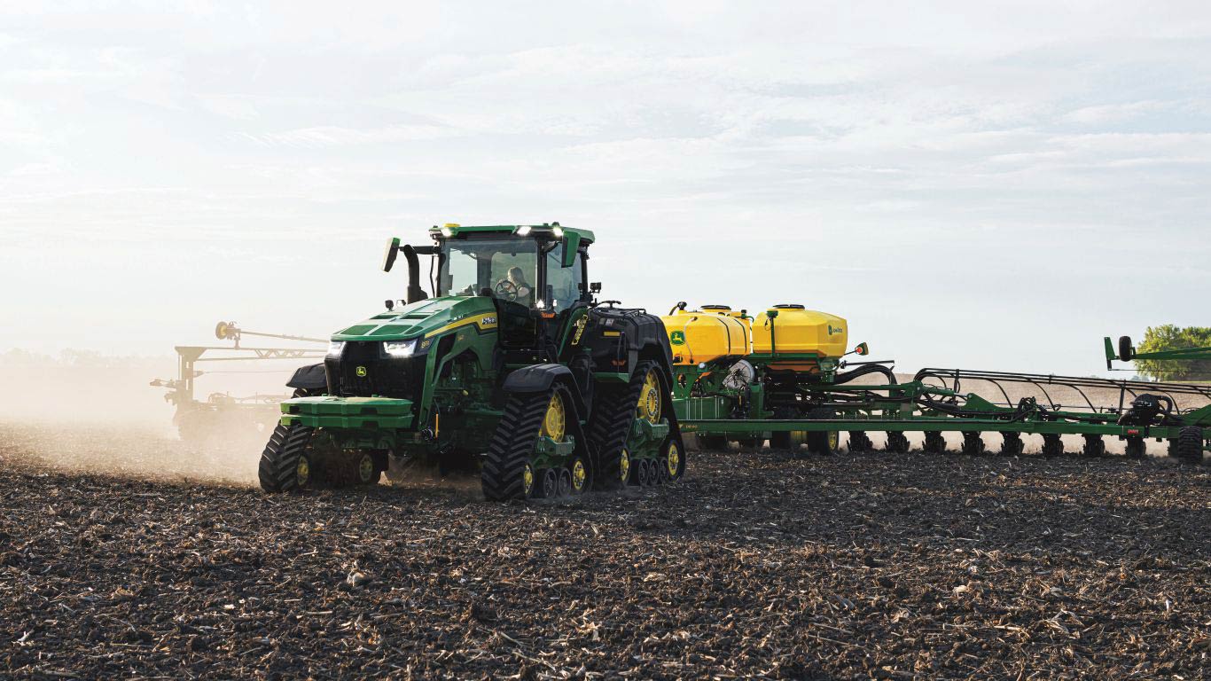 Green and yellow tracked wheeled tractor pulling a planting machine 