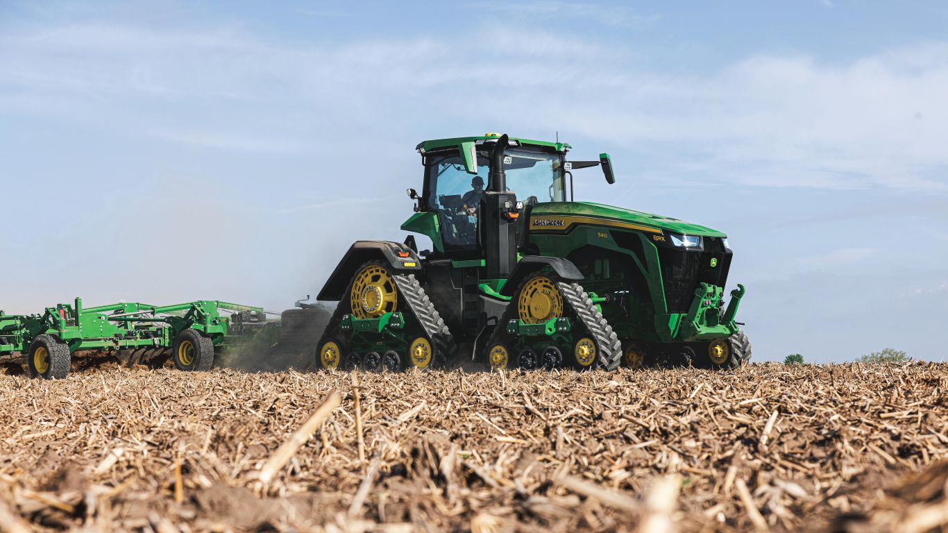 Large 8RX green and yellow tractor in brown field with blue sky