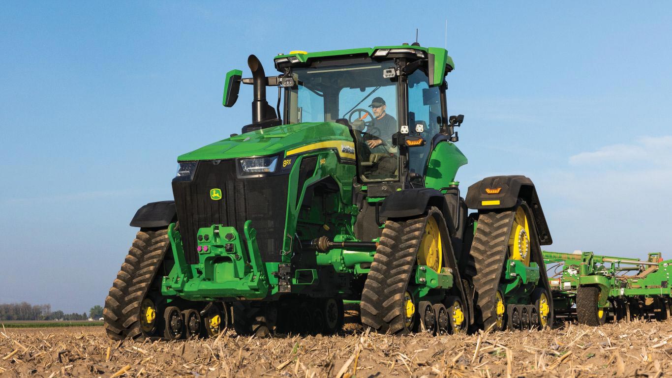 Large 8RX green and yellow tractor in brown field with blue sky