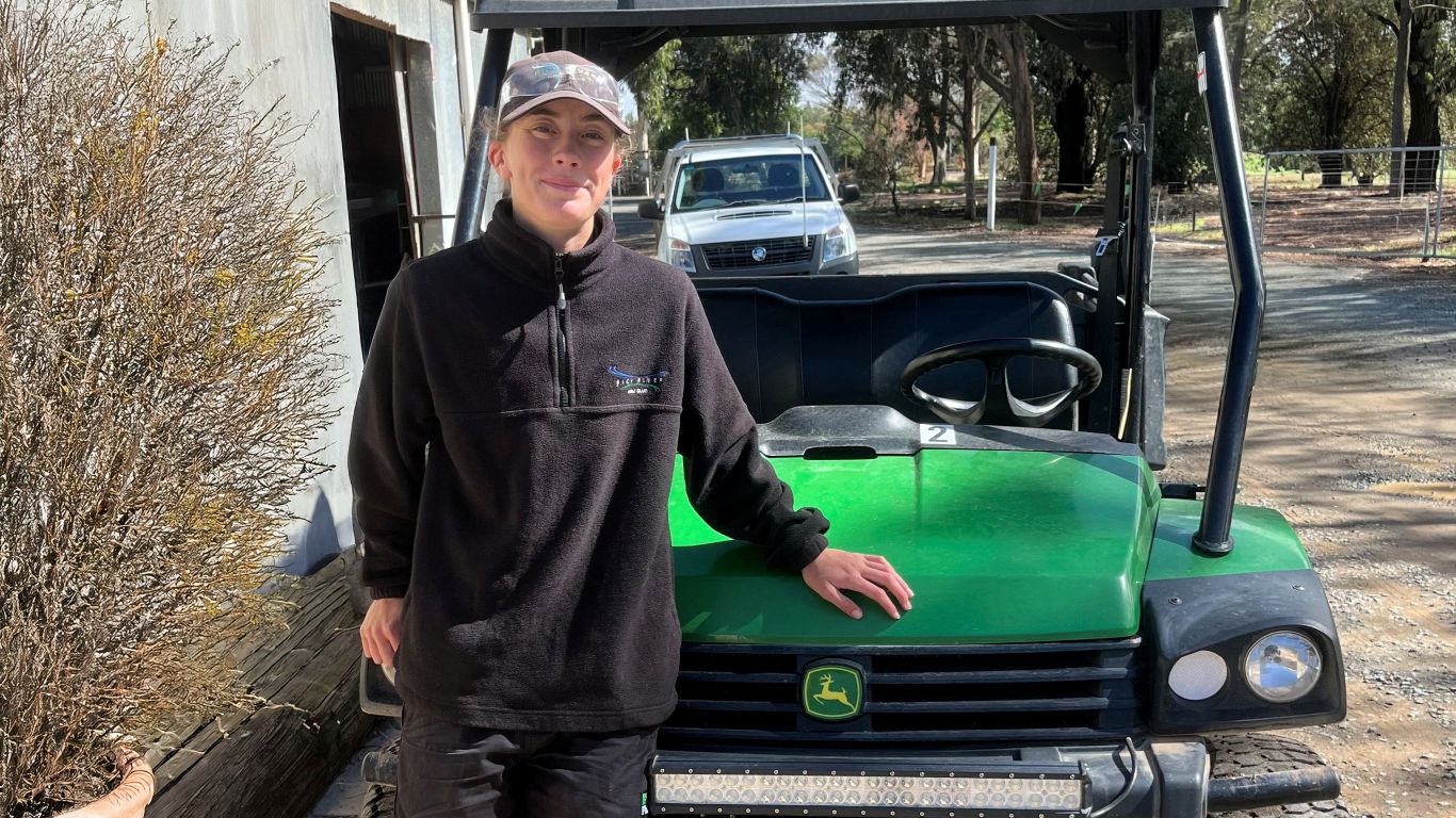 A lady wearing a black jumper and cap in front of a John Deere Gator.
