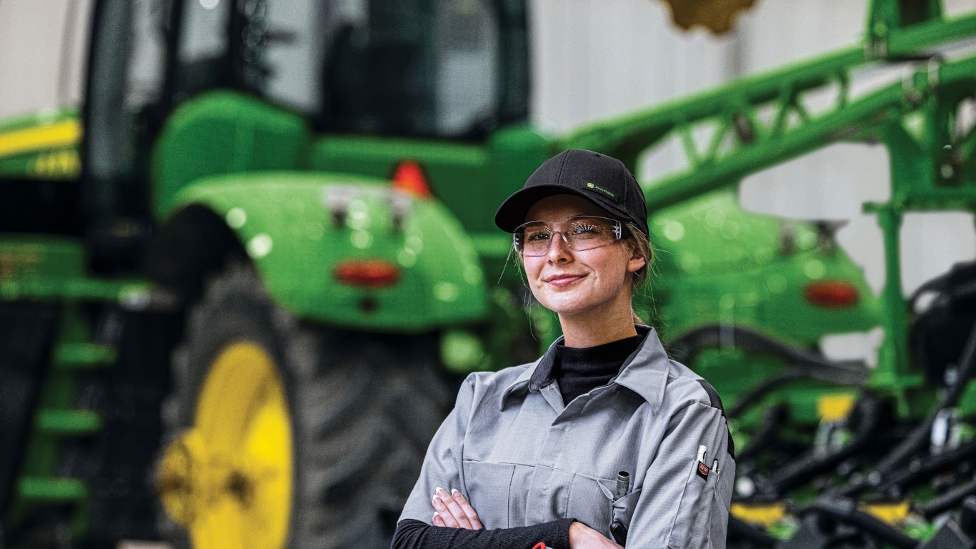 Grinning woman with safety glasses standing in front of an out of focus tractor