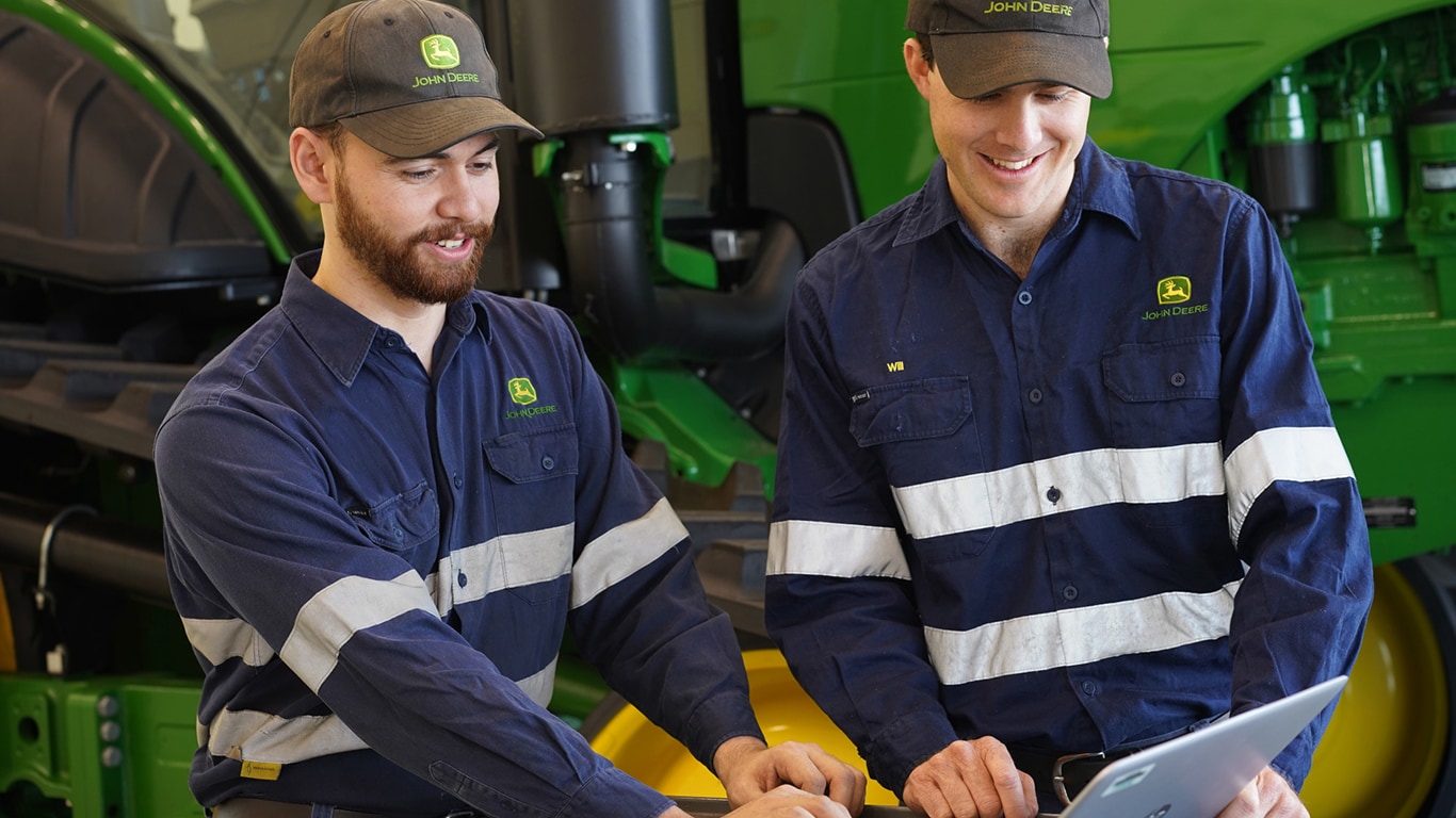 two men looking at a laptop next to a tractor