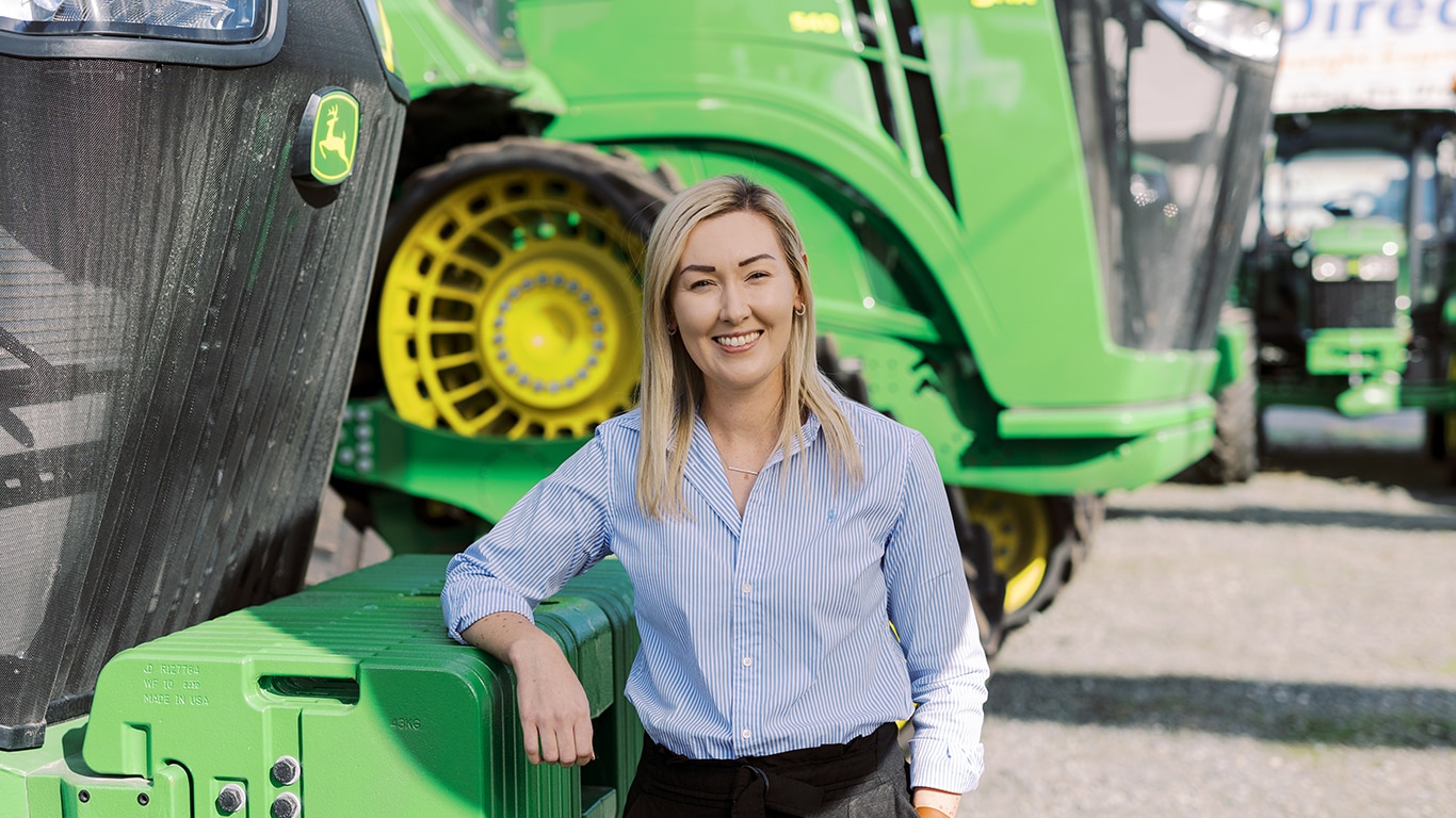 A John Deere employee smiling in front of a combine.