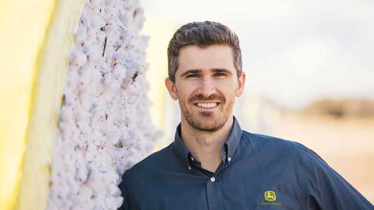 A John Deere employee smiling in front of a combine.