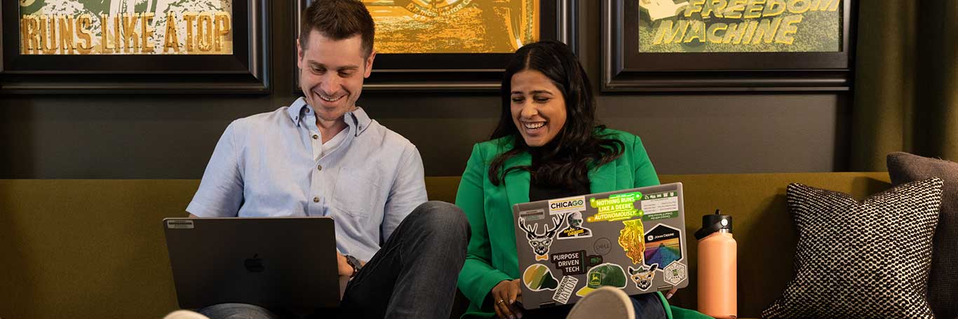 Two colleagues relax on a couch together while working on laptops