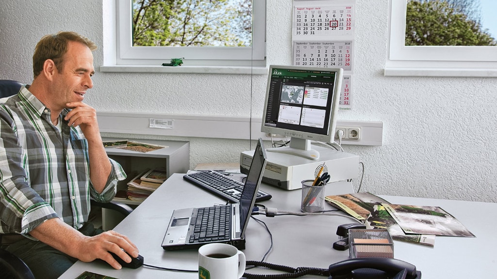a man smiling sitting in front of a monitor in an office