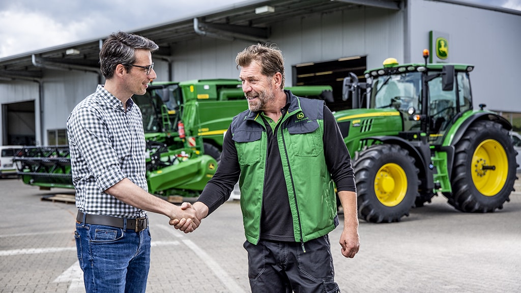 two men shaking hands in front of John Deere equipment at a dealership