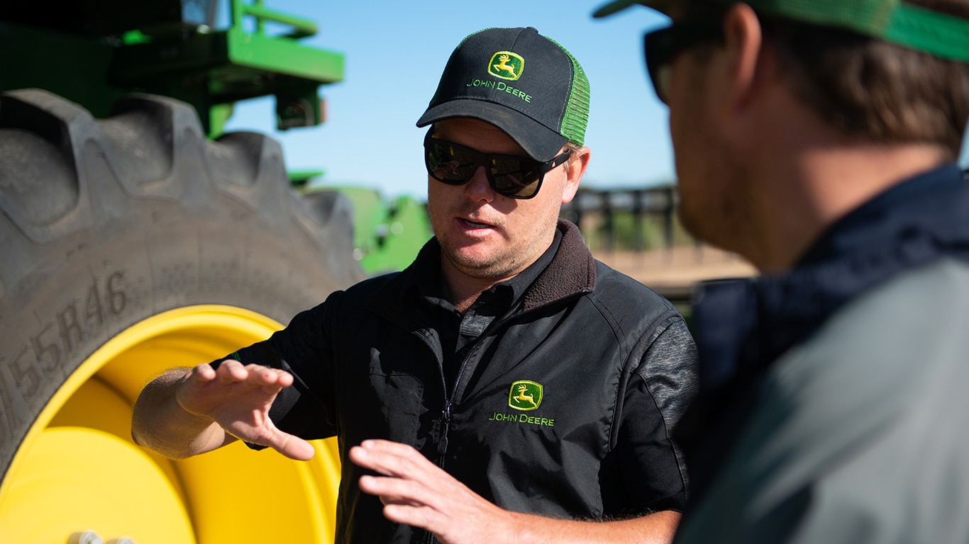 two men talking in front of John Deere equipment