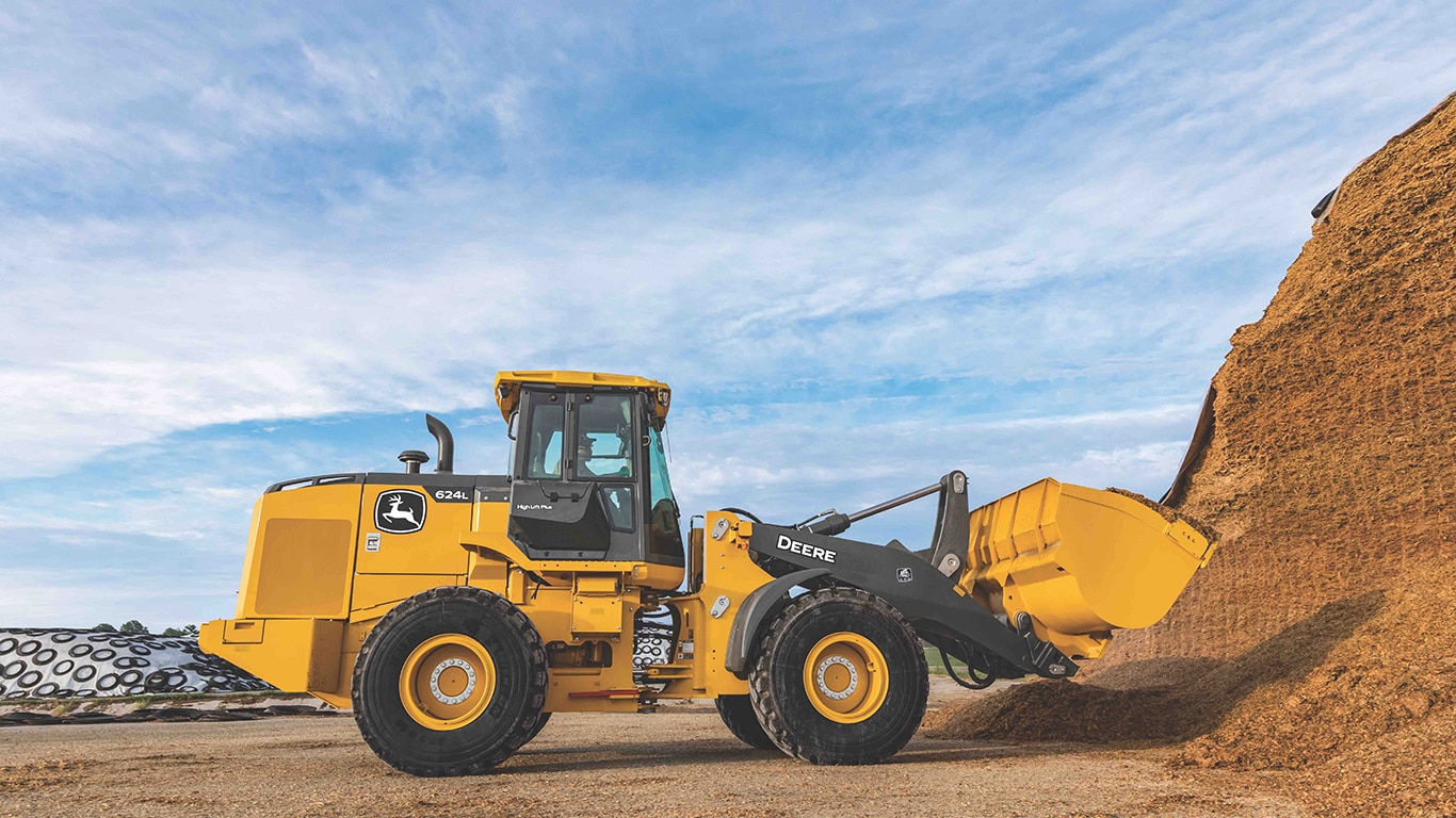 John Deere 624L Wheel Loader moving dirt in an open landscape with partly cloudy skies