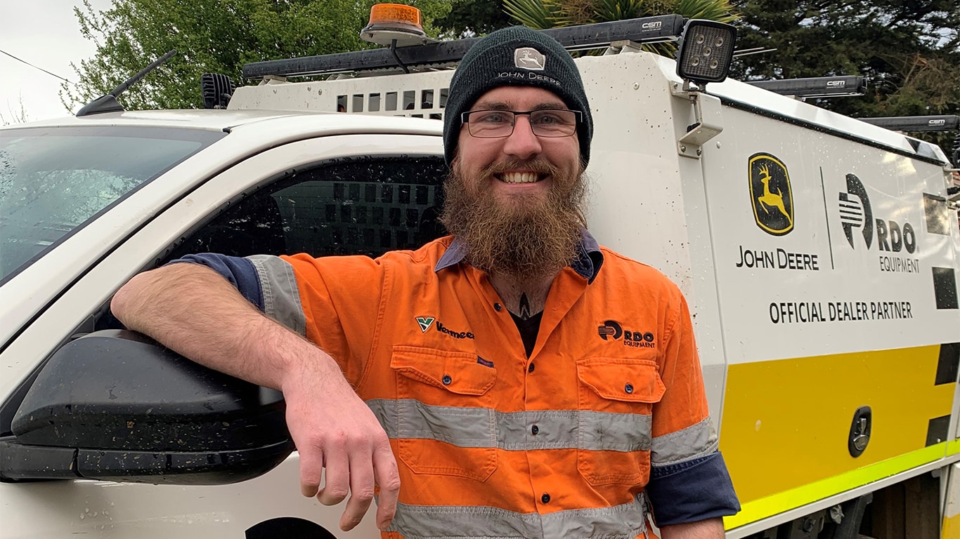 Brendan Wilkinson smiling beside a John Dear dealer truck