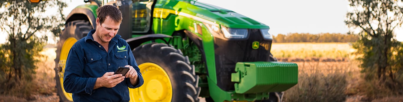 a man diagnosing problems on his phone in front of his tractor