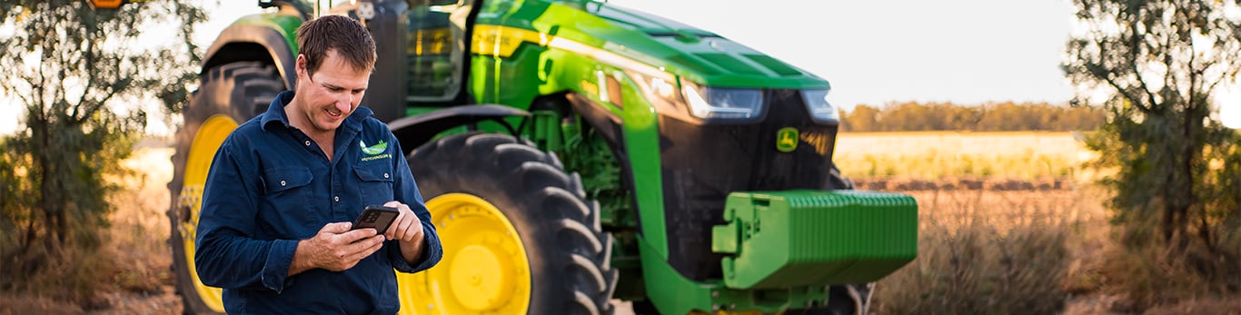 a man diagnosing problems on his phone in front of his tractor