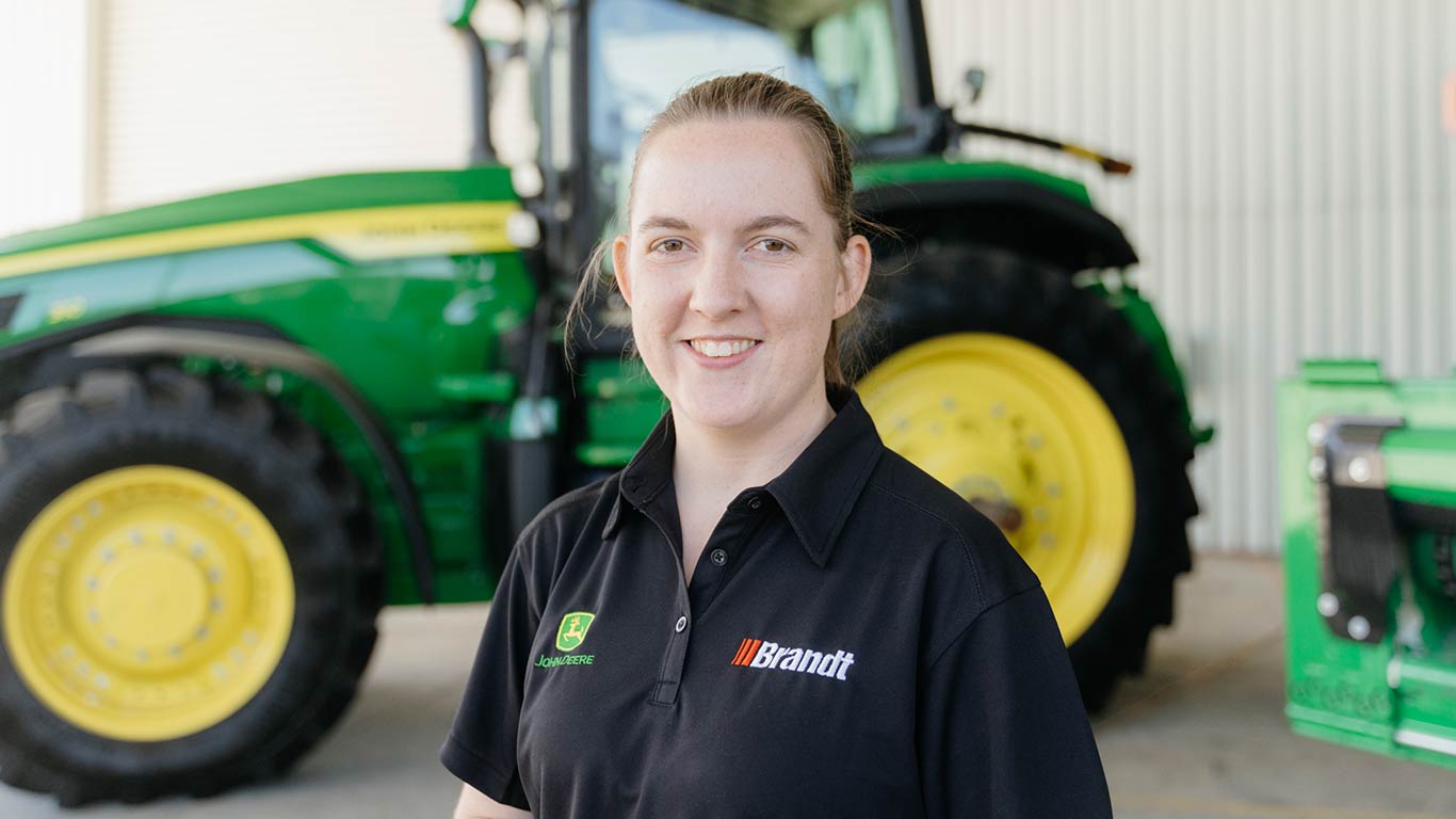 Kirsten Rush standing in front of green agriculture equipment, smiling at the camera.
