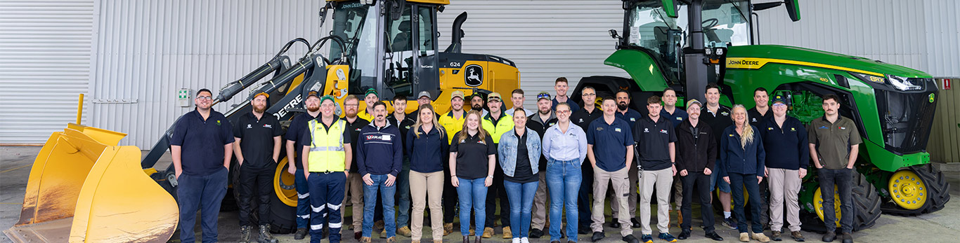 Group of employees standing between a John Deere loader and tractor inside a service facility.