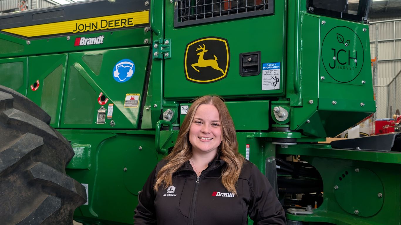 Person standing in front of a John Deere harvester inside a maintenance facility.