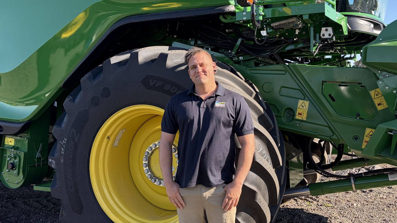Person standing beside a large John Deere agricultural machine with oversized rear wheel.
