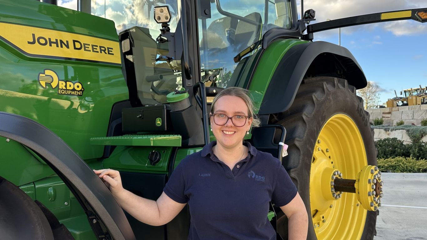 Person standing beside a John Deere tractor in an outdoor equipment dealership yard.