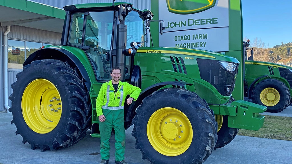 Greg smiling and leaning on Deere 6175M tractor