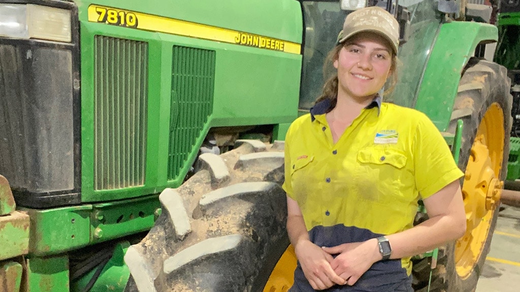 Jaymee smiling while leaning Deere 7810 tractor
