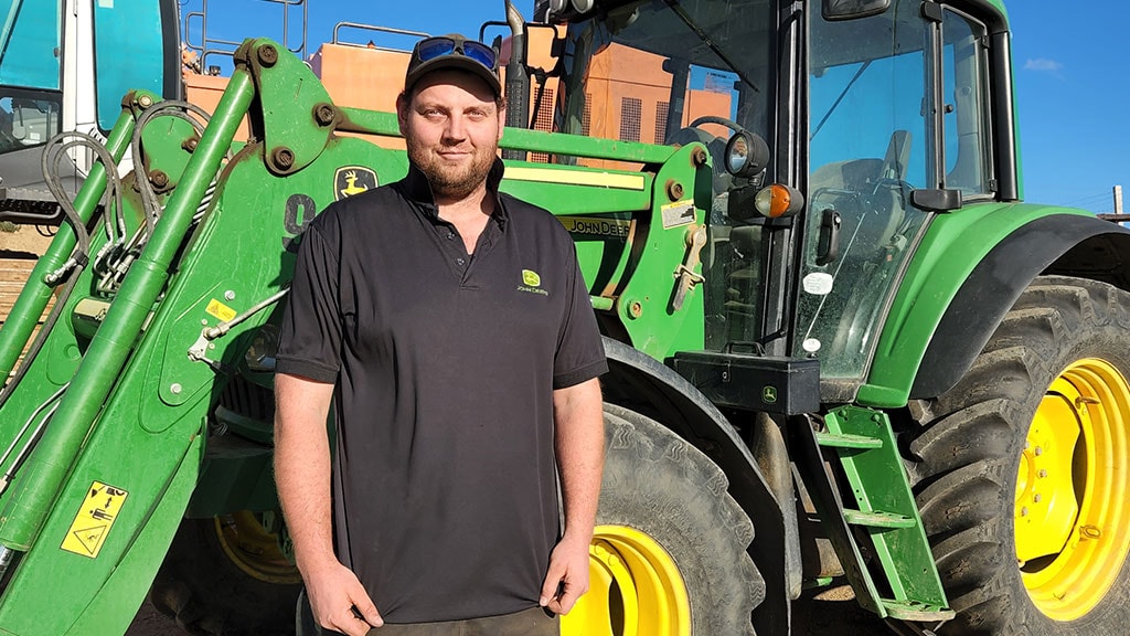 Logan smiling in front of Deere tractor with front loader