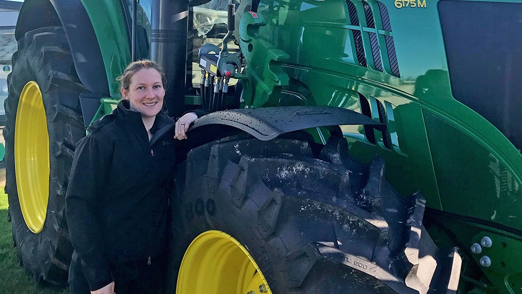 Megan smiling and leaning on Deere tractor