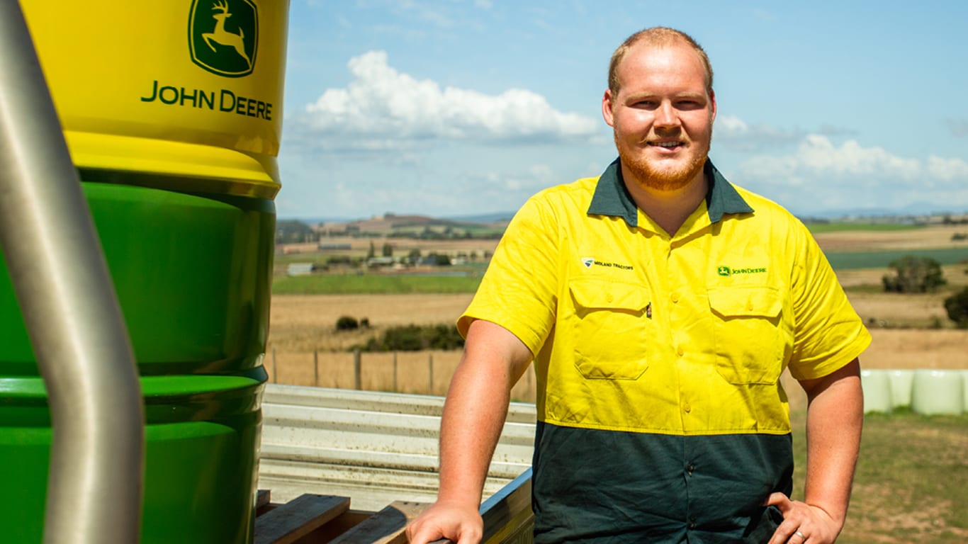 Caleb smiling next to a yellow and green barrel with the Deere logo on it