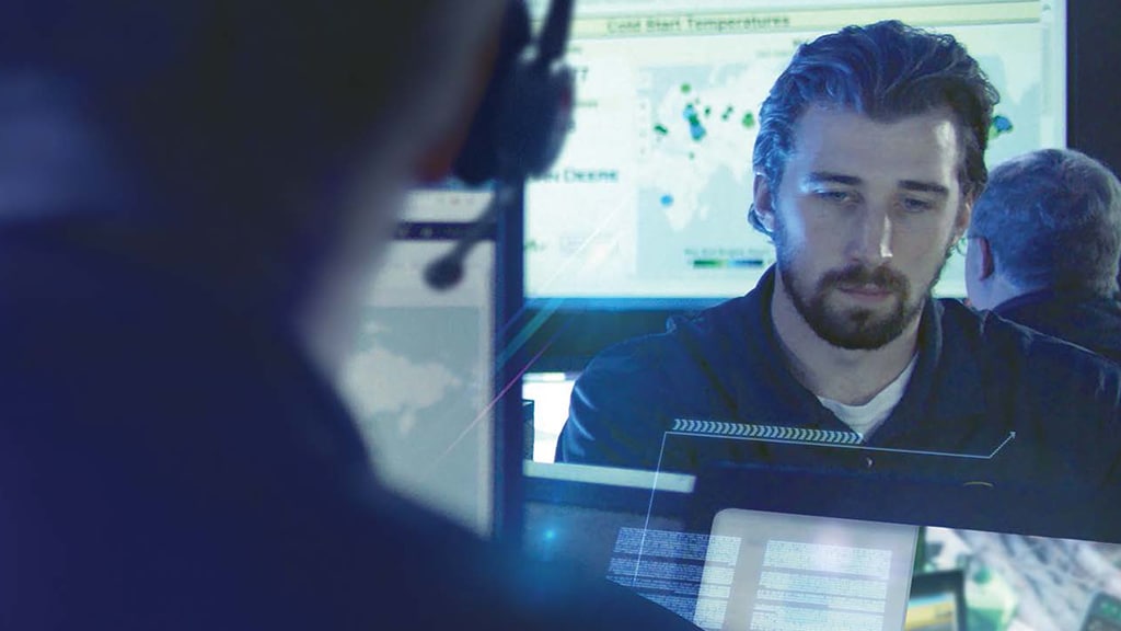 a focused worker looking at a computer in a blue lit room with others around also working on computers