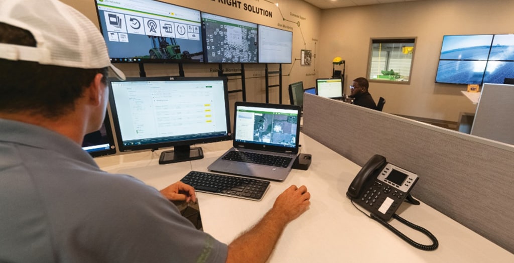 service technician sitting at a desk looking at a desktop computer in an office with several monitors on the walls