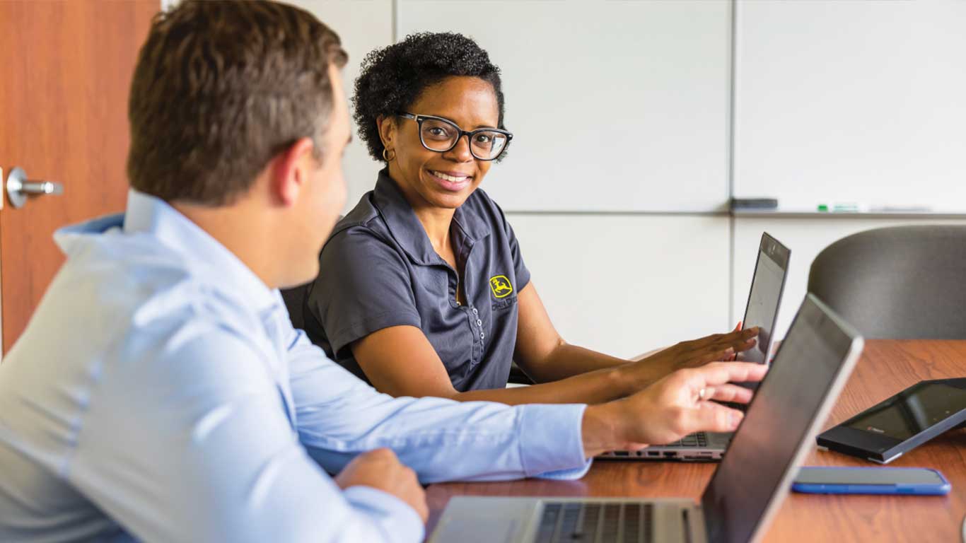 woman with specs and john deere T-shirt smiling while talking to another person