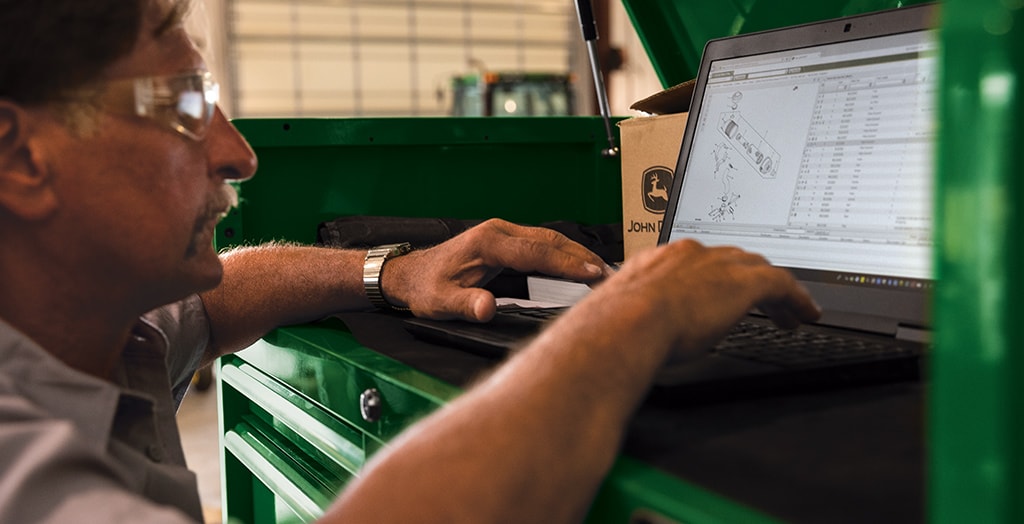 service technician wearing safety goggles working on a laptop set on a green mechanics bench