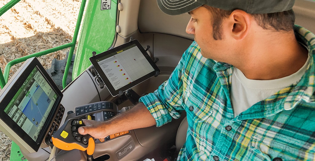 farmer sitting in a tractor cab with hand on a joystick looking at a monitor