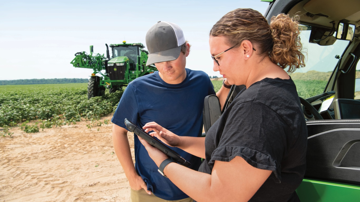 A man and a woman looking at a tablet in a field.