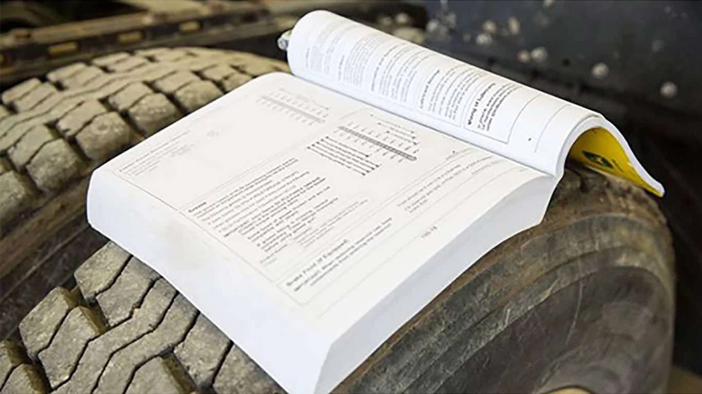 An open repair manual sitting atop a large vehicle tire.